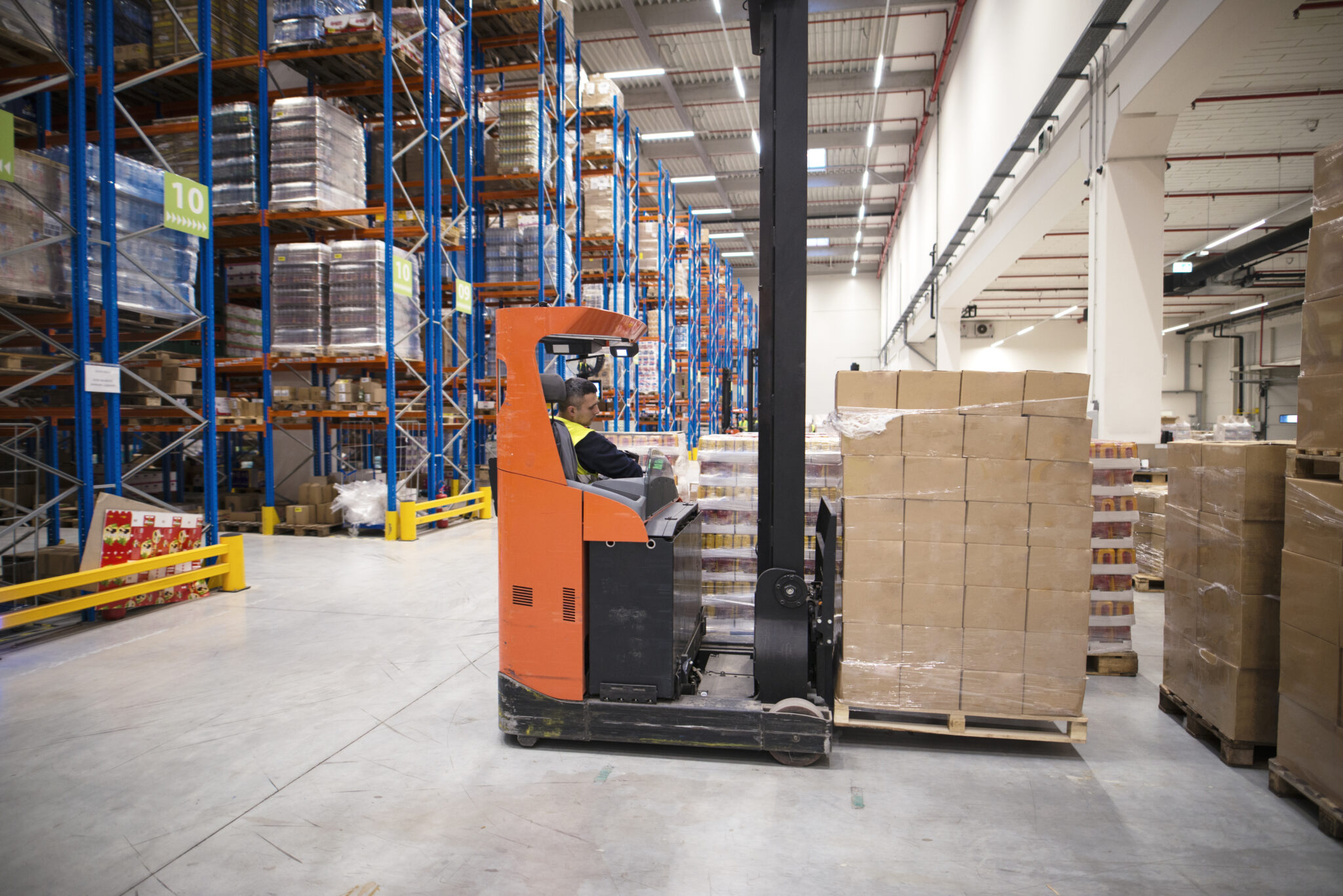 Industrial worker in protective uniform operating forklift in big warehouse distribution center.